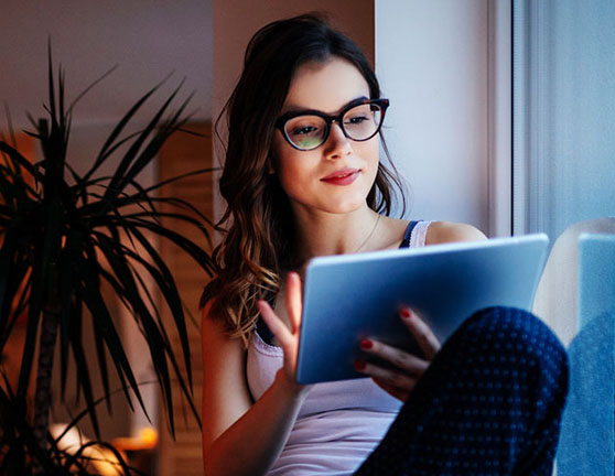 Mujer joven en el salón de su casa sujetando una tablet cerca de la ventana