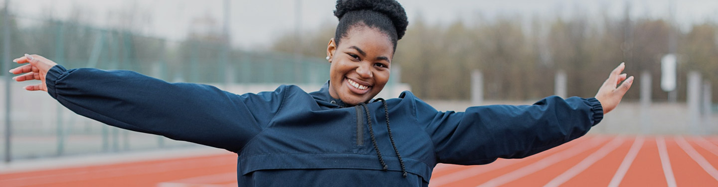 Mujer con los brazos abiertos con una pista de atletismo de fondo